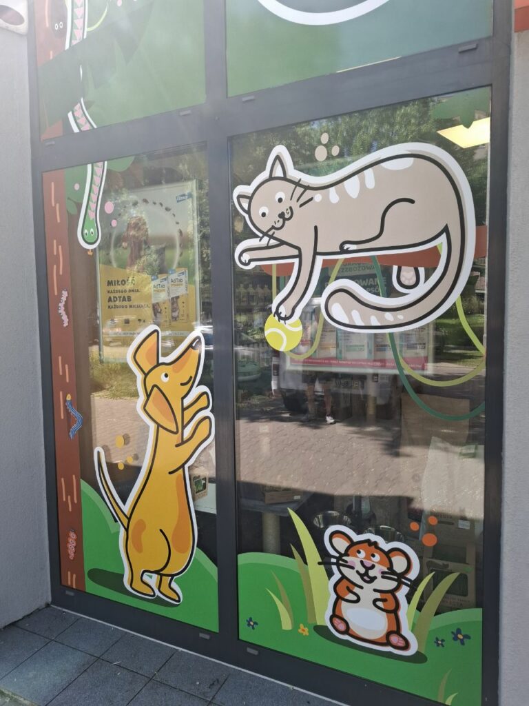 Oklejone szyby sklepu zoologicznego z grafikami psa, kota i chomika